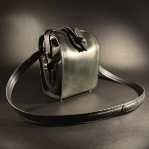 Luxury handstitched black and forest green doctor bag purse with hinged opening and unique push lock clasp of handles and strap view of front of closed purse with long strap