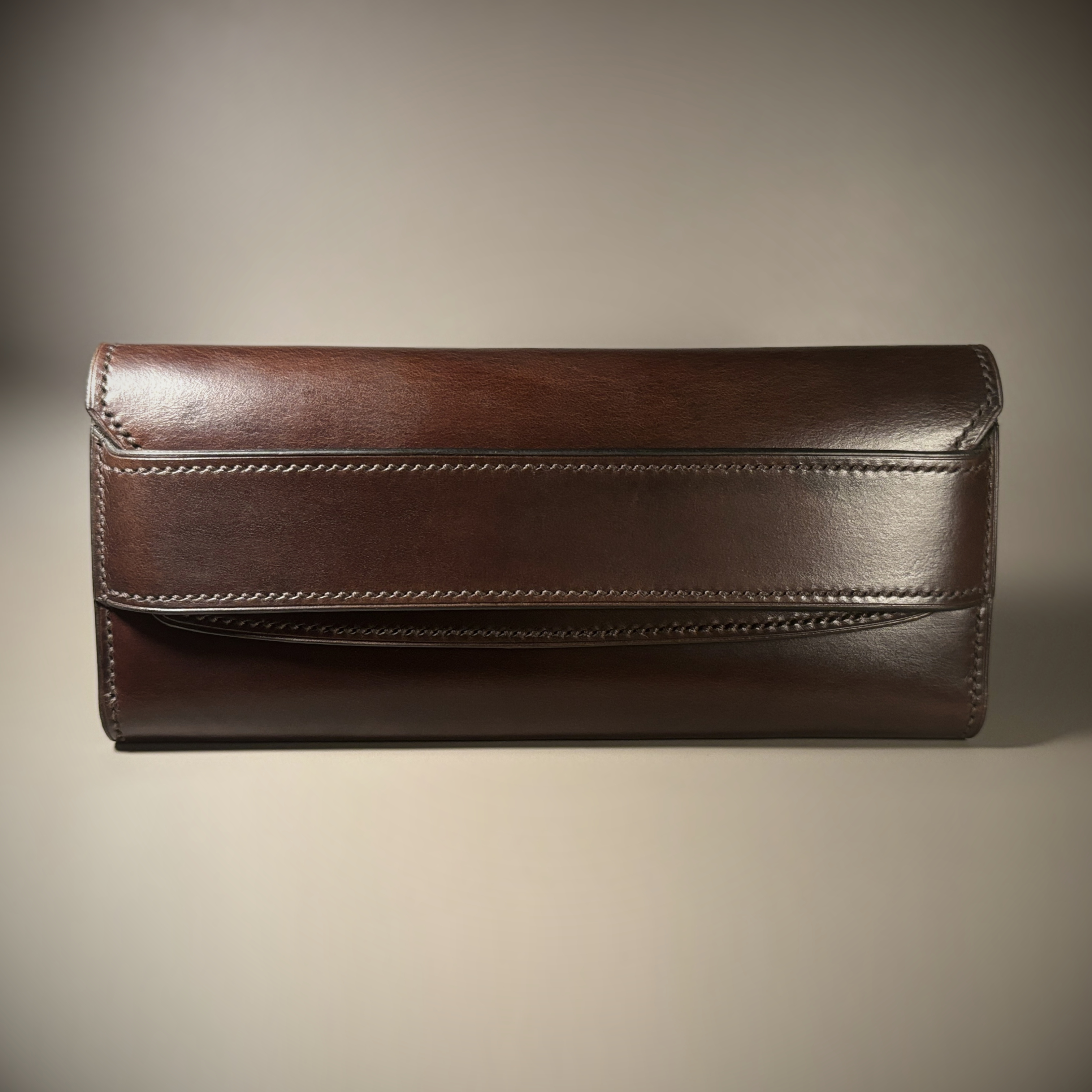 Unique handstitched tuck closure walnut shell and black and brown textured curved interior long wallet exterior font view