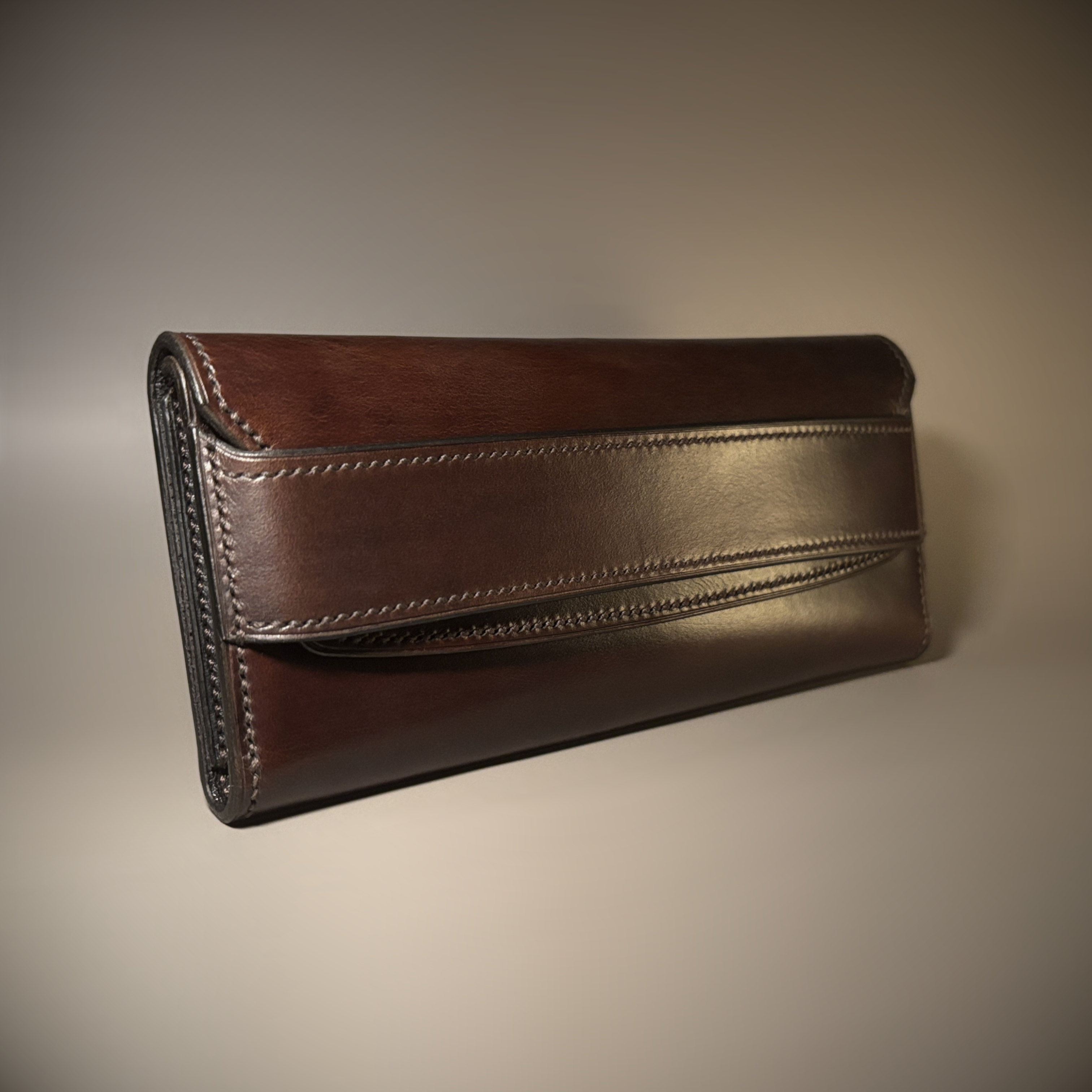 Unique handstitched tuck closure walnut shell and black and brown textured curved interior long wallet exterior side view