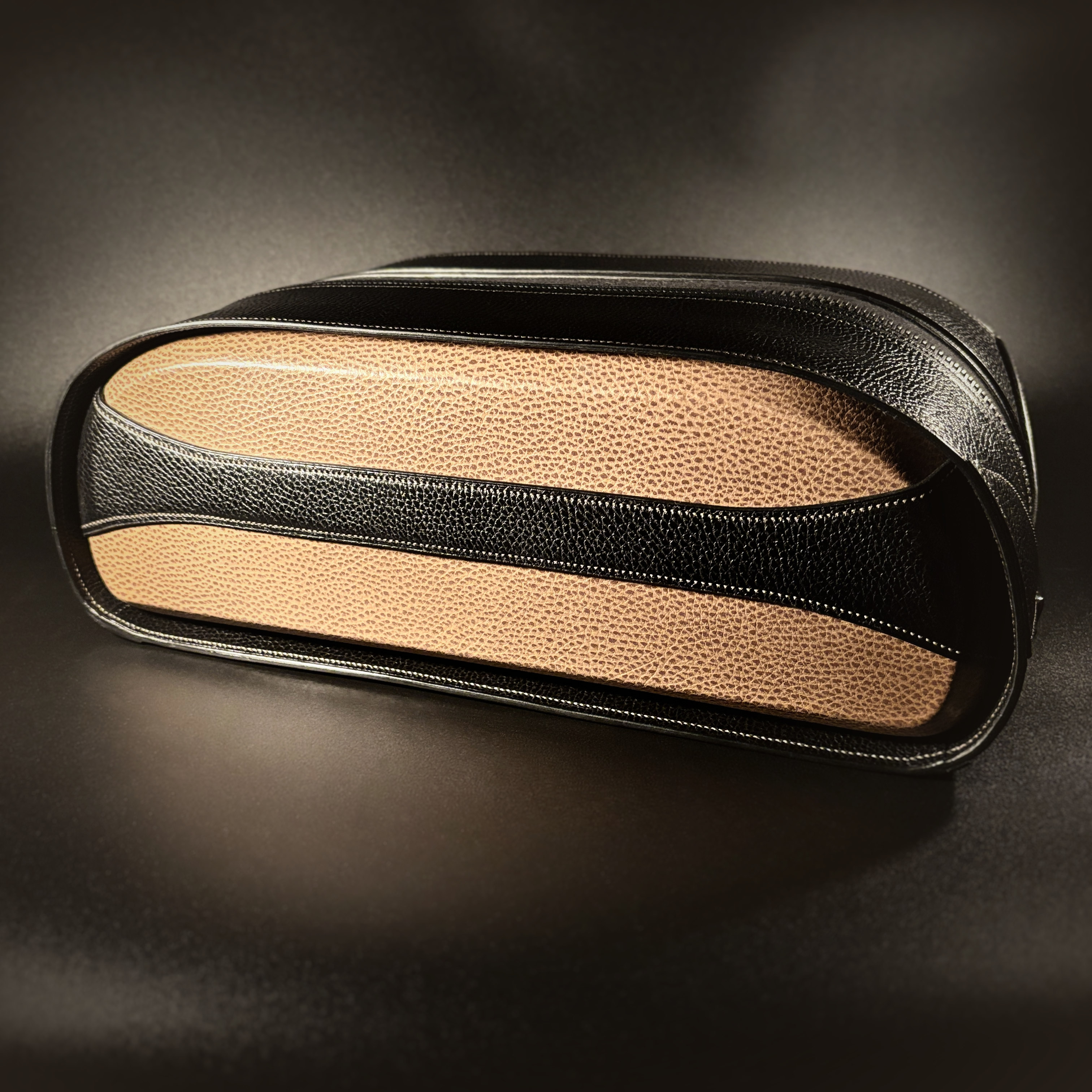 Luxury handstitched black and taupe leather messenger carryall bag with flowing curved design of handles and strap view of side with crossbody strap detached