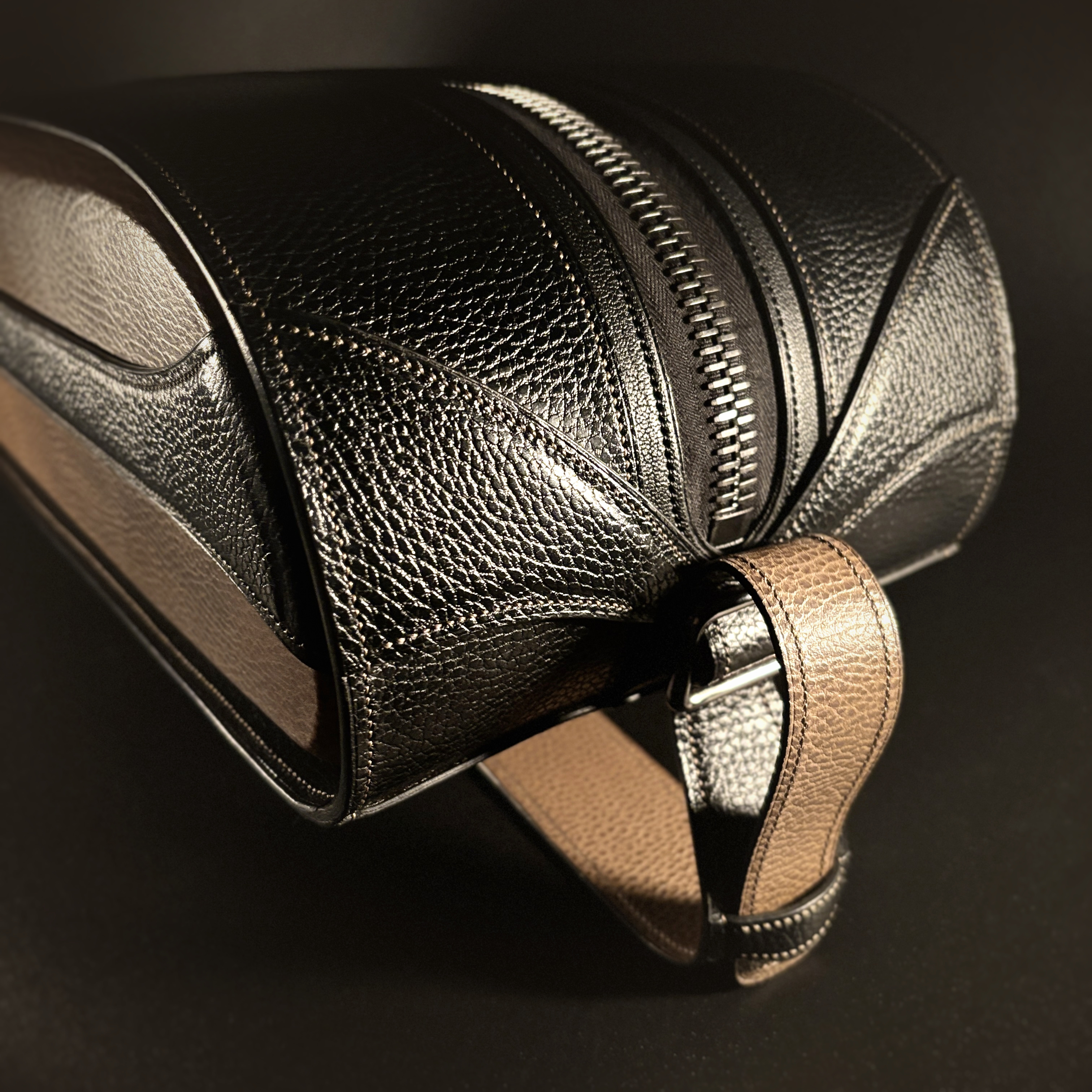 Luxury handstitched black and taupe leather messenger carryall bag with flowing curved design of handles and strap view of back and side with crossbody strap attached