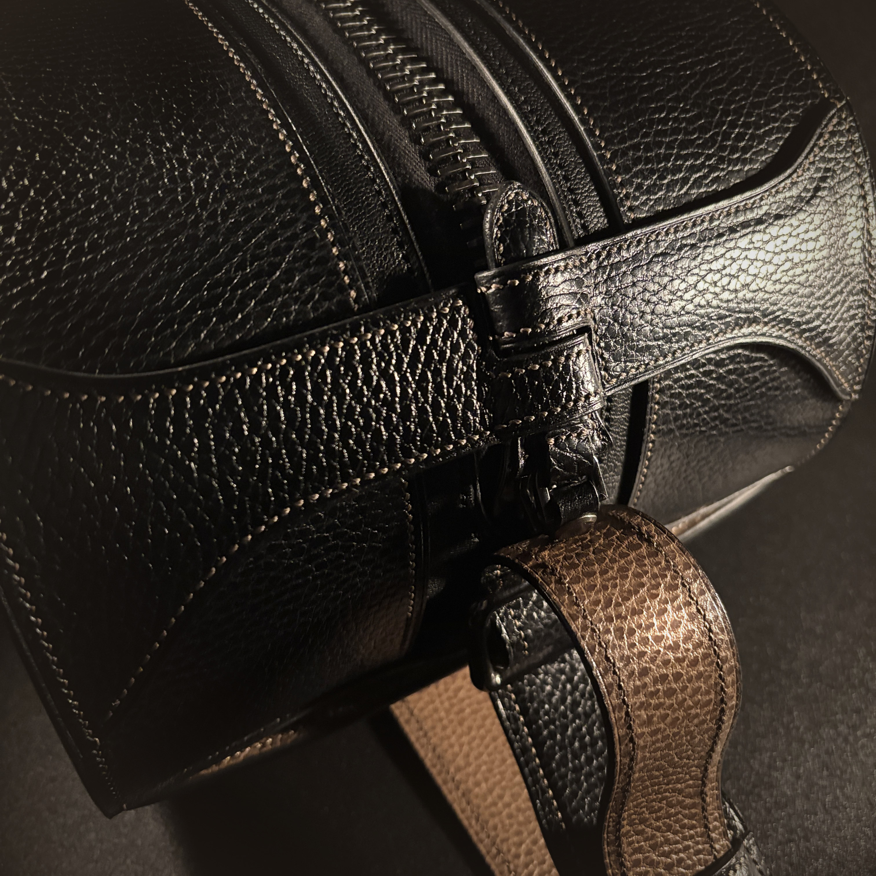 Luxury handstitched black and taupe leather messenger carryall bag with flowing curved design of handles and strap view of zipper pull closure closed