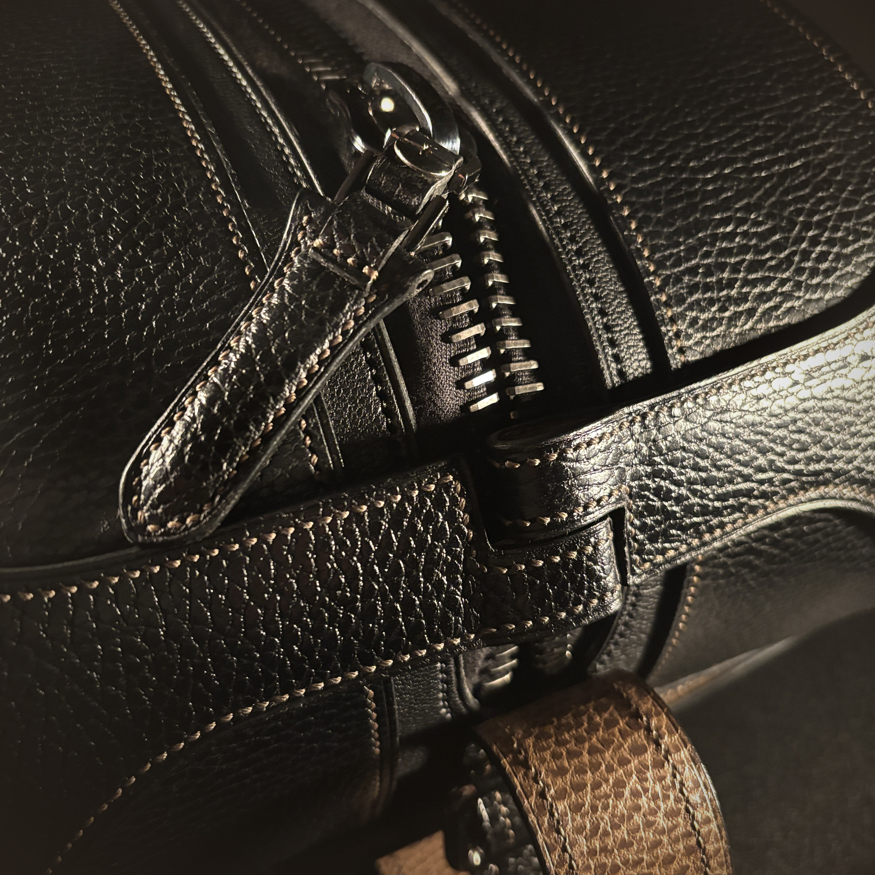 Luxury handstitched black and taupe leather messenger carryall bag with flowing curved design of handles and strap view of zipper pull closure open