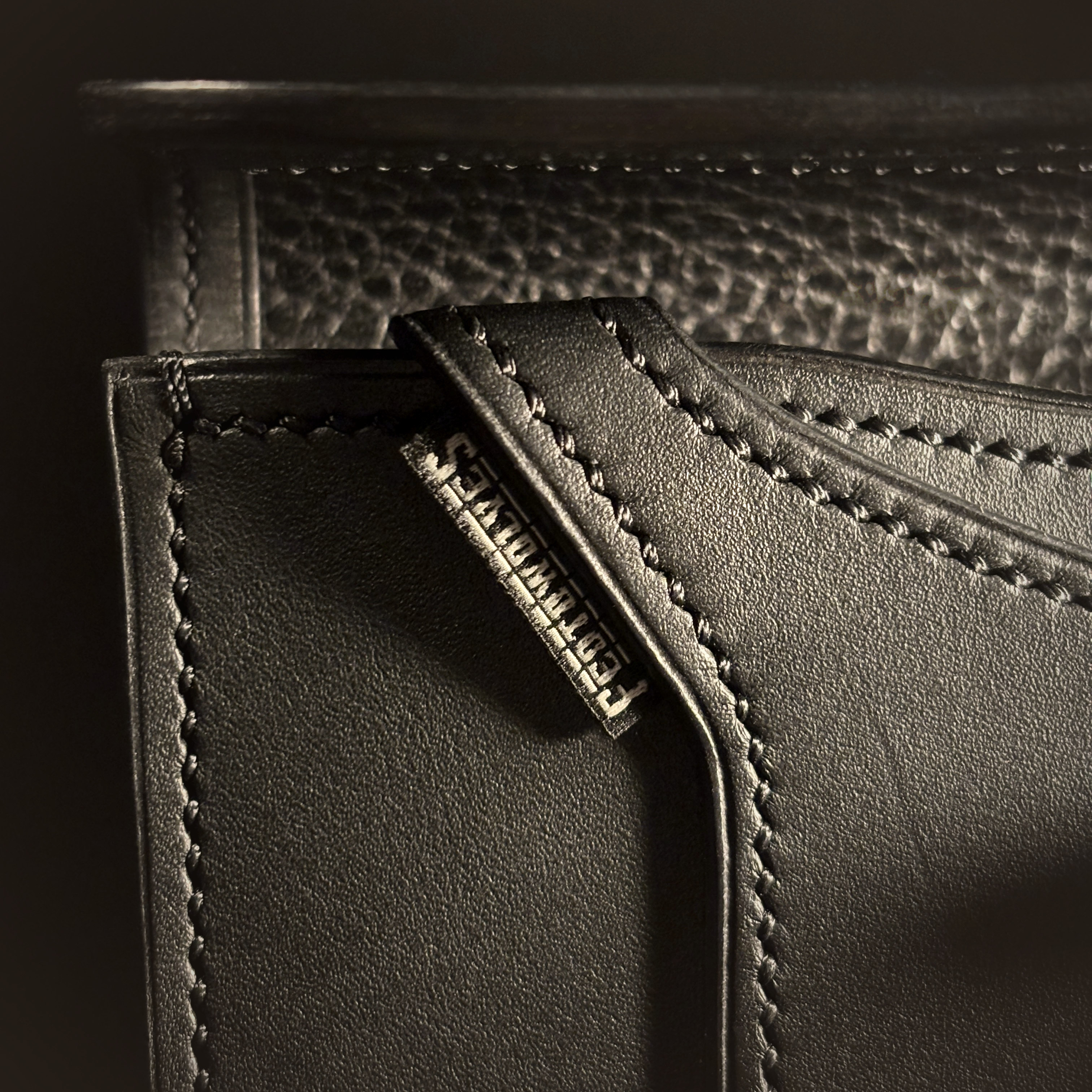Luxury handstitched matte black clutch purse with unique tab closure detailed view of intricate hand stitching