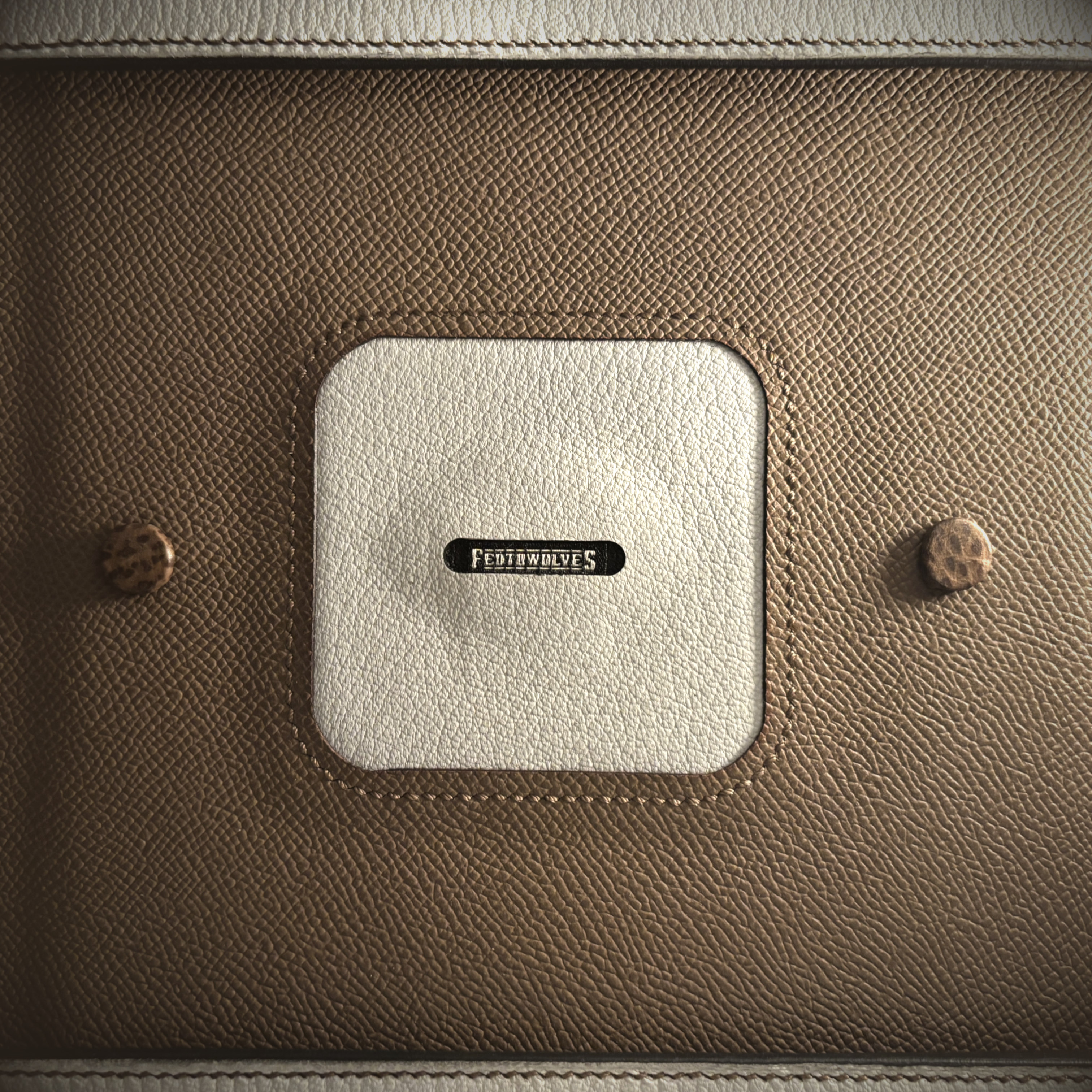 Luxury handstitched black and taupe leather messenger carryall bag with flowing curved design of handles and strap view of taupe and white interior base with Fed To Wolves tag stitched into square cutout detail