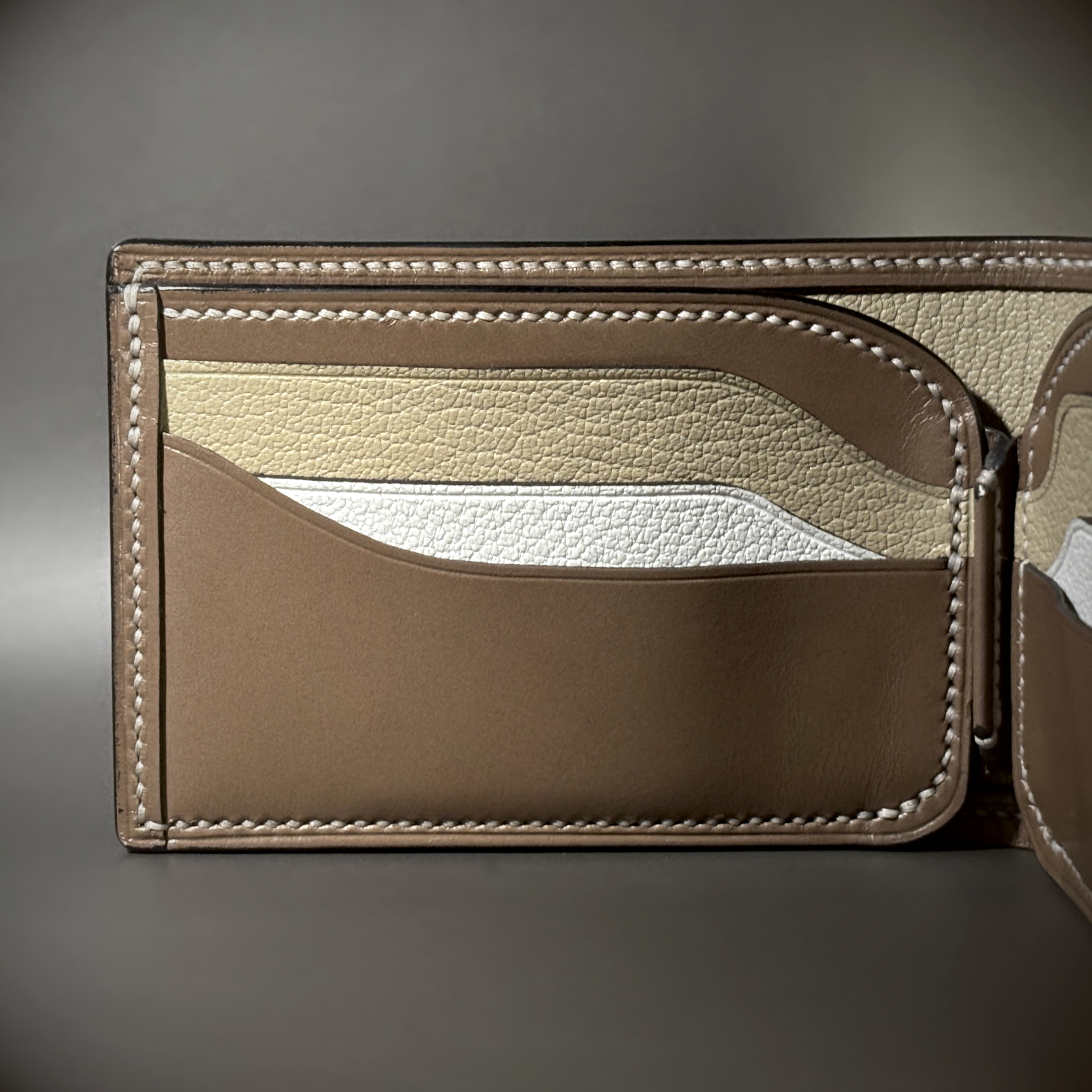Tan taupe and white bifold wallet with black shell handstitched with white thread detailed view