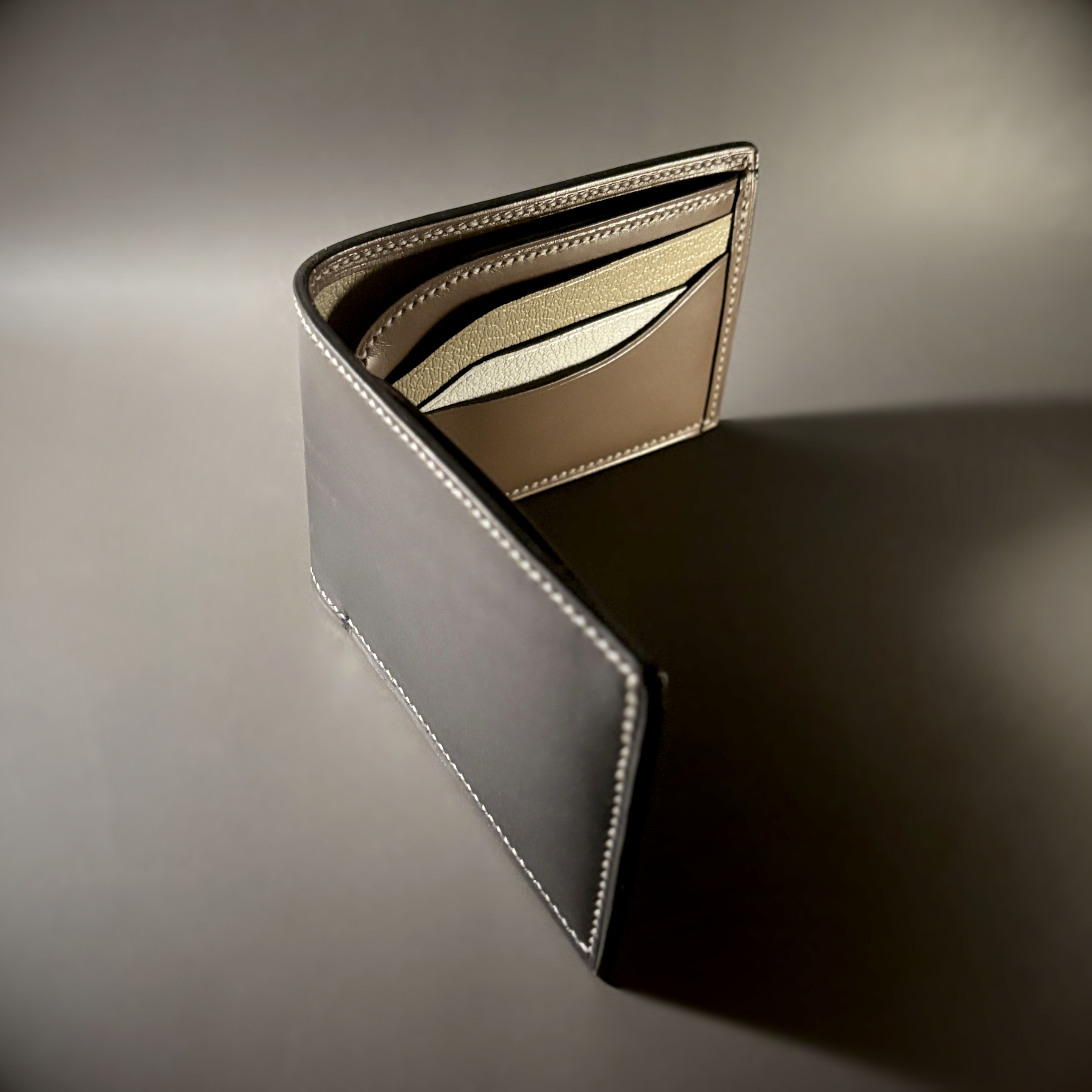 Tan taupe and white bifold wallet with black shell handstitched with white thread side view